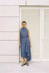 Vestido midi de color azul, confeccionado con lino. Presenta cuello redondo, manga sisa y diseño sin mangas. Cuenta con bajo asimétrico y detalle de vuelo en la parte frontal.