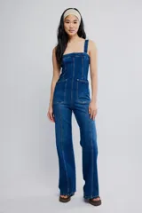 Mameluco de denim elastizado azul, entallado en el cuerpo con pierna bootcut. Presenta escote cuadrado, bolsillos plaqué delanteros, tiras anchas y cierre en la espalda.