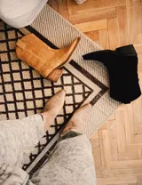 Bota corta de gamuza color marrón topo, estilo western, con bordados decorativos en hilo blanco en caña y empeine. Posee taco cuadrado de madera y punta ligeramente afilada.