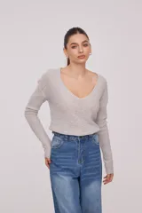 Sweater de tejido de punto fino, color beige, con escote en V profundo y mangas largas. Presenta un corte holgado y diseño minimalista.