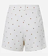 Bermuda de piquet color blanco con estampado de lunares negros, de corte recto, tiro alto, con trabillas en la cintura, pliegues y cierre tradicional.