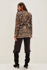 Saco sastrero con escote en V y mangas largas, confeccionado en gabardina liviana negra con bordados florales y patrones geométricos en tonos beige, dorado y toques de color (fucsia, verde, violeta). Presenta botones ocultos, bolsillos ojal, hombreras y un cinturón fino de cuero negro.