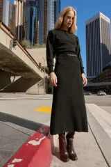 Vestido midi de punto en color negro, con cuello barco y mangas largas con sisa ancha. Presenta una cintura entallada con un cinturón fino incorporado con hebilla metálica dorada.