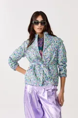 Chaqueta capitoneada con estampado floral y terminación metálica, cuello alto, cierre frontal escondido, cinturón para atar y bolsillos laterales.