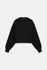 Jersey corto de punto liso, con cuello redondo y manga larga con puños ajustados. Presenta un diseño de corte crop con aberturas laterales en el bajo.
