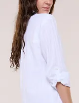 Vestido camisero corto de color blanco con sutiles rayas verticales, de la marca Dash. Presenta cuello con solapa, escote en V con botones parciales en el frente, bolsillo superior en el pecho y bolsillos laterales de gran tamaño. Cuenta con mangas largas de largo regulable mediante presilla y botón, calce holgado y ruedo trasero más largo.
