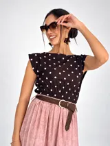 Blusa sin mangas de viscosa color negro con estampado de lunares blancos, cuello redondo y cintura fruncida con elástico.