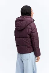 Campera puffer negra con capucha, diseño corto y acolchado, cierre frontal con botones a presión y puños ajustados.