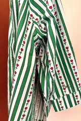 Camisa de manga larga con cuello clásico y cierre frontal de botones. Presenta un diseño de rayas verticales verdes y blancas con un estampado lineal de pequeñas flores rojas.