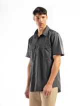 Camisa de manga corta color gris oscuro, con cuello clásico, cierre frontal con botones, dos bolsillos de parche con solapa abotonada en el pecho y corte recto.