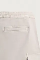 Bermuda cargo color negro de corte relaxed fit, confeccionada en tejido de algodón con elasticidad y efecto lavado. Cuenta con cintura elástica ajustable con cordón, bolsillos frontales y bolsillos laterales tipo cargo con solapa en las perneras.