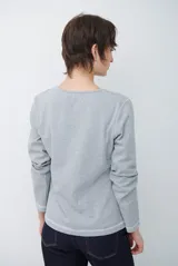 Remera de manga larga con cuello redondo, confeccionada en tejido de punto gris melange con costuras visibles en contraste.