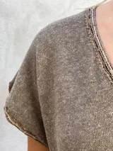 Vestido midi de tejido de punto color marrón, con cuello en V y mangas cortas. Presenta un diseño holgado y un detalle decorativo de crochet con formas circulares en el ruedo.