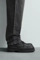 Bota tipo derby con cordones, confeccionada en material liso con horma redonda. Presenta una suela con volumen y piso track dentado.