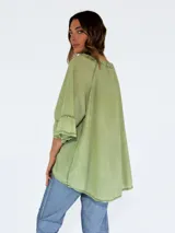 Blusa verde oliva de corte holgado, con cuello redondo con volantes y abertura en V con lazo. Tiene mangas 3/4 acampanadas y ruedo asimétrico.