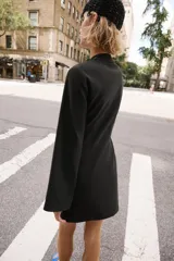 Vestido corto negro de cuello mao y escote en V, con mangas largas abanicadas y cierre de alamares en el frente. Cuenta con bolsillos frontales de plastrón y diseño de inspiración oriental.