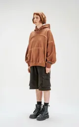 Hoodie oversize color beige con efecto batik, costuras expuestas y recortes estructurales. Presenta capucha amplia y bolsillo frontal tipo canguro.