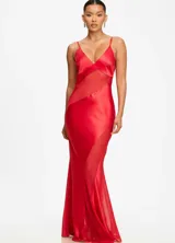 Vestido largo de satén rojo con paneles de mesh transparente estratégicamente ubicados. Presenta escote en V con breteles finos y una silueta fluida que se ajusta al cuerpo.