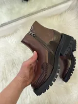 Bota corta de cuero color chocolate con suela track negra. Presenta una combinación de texturas que incluye cuero liso, gamuza y detalles con textura de reptil en la puntera y el talón.
