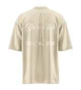 Remera de corte relajado y holgado en color beige, con diseño estampado en la espalda que presenta la frase 'Dropz Corp.' en tipografía cursiva sobre la silueta lineal de un ángel, acompañada de microtexto y un código de barras gráfico en la parte inferior.