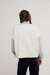 Buzo de frisa con diseño colorblock en tonos blanco y gris, cuello alto con botones a presión frontales, mangas largas raglán y puños y cintura acanalados.