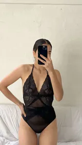 Body de encaje y microtul negro con diseño de escote halter, espalda descubierta y cierre con ganchos. Presenta paneles de encaje floral y secciones de tul transparente.
