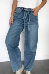 Pantalón de jean estilo mom fit en tono azul clásico, con diseño de tiro alto y lazo ajustable en la cintura. Presenta un corte relajado y holgado en las piernas, confeccionado en denim rígido con estructura.