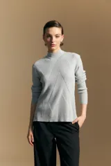 Polera de cuello alto en color blanco, confeccionada en tejido acanalado con un diseño geométrico de relieve que crea un efecto visual estilizado. Presenta un corte al cuerpo y mangas largas, ideal para usar como prenda base o principal.