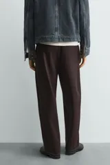 Pantalón de hombre color marrón oscuro, de corte balloon fit, con cintura con trabillas y cierre frontal de botón y cremallera. Presenta bolsillos delanteros y bolsillos traseros de vivo.
