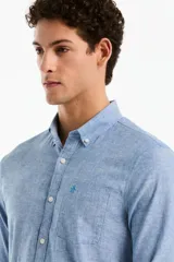 Camisa de manga larga confeccionada en mezcla de lino y algodón, color celeste melange, con cuello camisero abotonado, cierre frontal de botones y un bolsillo aplicado en el pecho con el logo bordado.