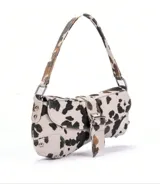 Cartera baguette con estampado de vaca en blanco y negro, con correa de hombro y cierre con hebilla metálica.