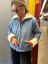 Campera de jean celeste con interior y cuello de corderito color crema, cierre frontal con cremallera y bolsillos laterales.