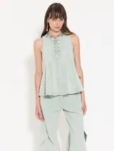 Top sin mangas color celeste claro, confeccionado en gabardina, con escote delantero ajustable mediante cordón y ojalillos. Presenta recortes triangulares que generan vuelo en la parte inferior.