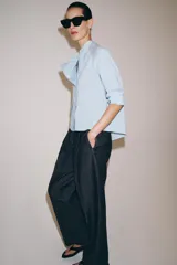 Camisa de corte oversize con estampado de rayas verticales, cuello redondo tipo mao y cierre frontal con botones. Presenta manga larga con puños anchos, un bolsillo de plastrón con solapa en el frente y bajo asimétrico.