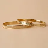 Esclava rígida de oro 18k con acabado satinado y diseño de cinta plana. Presenta una textura fina en su superficie y un diseño minimalista.