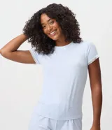 Blusa de pijama de mujer color celeste, confeccionada en tejido peach touch de poliéster con elastano, con estampado de moños sutiles. Presenta cuello redondo, mangas cortas con detalles de encaje blanco y un pequeño moño decorativo en el escote.