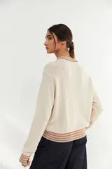 Bomber de tejido de punto color crudo, con cierre frontal completo y detalles de franjas multicolores en cuello, puños y ruedo.