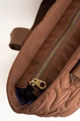 Bolso tipo tote bag color marrón con diseño capitonado de ondas, asas largas y placa metálica con el logo de la marca.