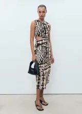 Vestido midi sin mangas con cuello redondo y aberturas laterales tipo cut-out en la cintura. Presenta un diseño recto con estampado botánico en contraste y cierre de cremallera en la parte posterior.