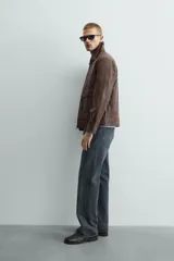 Sobrecamisa de corte relajado confeccionada en tejido efecto piel color marrón. Presenta cuello solapa, cierre frontal con cremallera, mangas largas con puños abotonados y dos bolsillos de plastrón con solapa en la parte frontal.