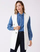 Chaleco largo tejido color blanco de la marca Sioni, con cuello solapa, doble botonadura dorada en el frente y bolsillos aplicados.