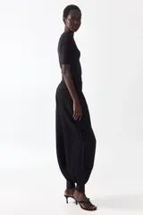 Pantalón de sarga negro de tiro alto con bolsillos laterales discretos y cierre con botón y corchetes ocultos. Presenta diseño de piernas globo con pinzas y puños abotonados con frunces.