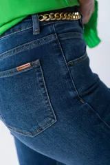 Pantalón de jean azul de corte recto con terminación desflecada y cadena dorada decorativa.