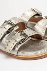 Sandalias de cuero color negro con dos tiras anchas sobre el empeine, cada una con hebillas metálicas ajustables y detalles de tachas plateadas. La suela es de cuero con un borde de color madera.