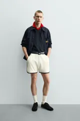Short deportivo de tejido de punto con estructura abierta, color blanco con vivos a contraste en azul marino. Presenta cintura elástica, bolsillos frontales, aberturas laterales en el bajo y etiquetas conmemorativas de la Copa Mundial de la FIFA Francia 98.