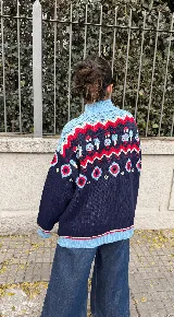 Buzo de punto grueso con cuello alto y diseño jacquard que presenta motivos de granjeros, casas y árboles en tonos crema, marrón, rojo y amarillo.