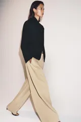 Pantalón de tiro medio con corte wide leg, confeccionado en algodón. Presenta cintura con trabillas, bolsillos laterales ocultos y detalle de pliegues en el delantero. Cierre frontal con cremallera, botón y ganchos metálicos.