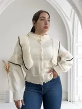 Cárdigan tejido color crudo con cuello redondo, cierre frontal con botones y mangas abullonadas con puños acanalados y detalle de rayas negras.