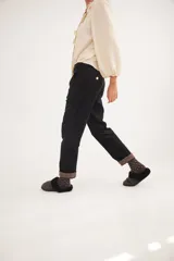 Pantalón de corte recto y tiro medio, confeccionado en pana fina con lycra. Presenta pinzas frontales, bolsillos laterales y traseros, y un botón metálico en tono oro. El diseño destaca por el detalle de paño espigado en el interior del ruedo, visible al doblarlo.