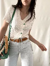 Camisa blanca con textura arrugada, escote en V, mangas cortas con volados y botones con forma de flor.